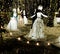 Woman figures dancing in white dresses under bright string lights on the snow. Christmas theme installation