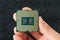 Woman fingers hold pc micro CPU with gold plated contacts against dark background. Modern central processing unit close-up.