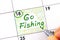 Woman fingers with pen writing reminder Go Fishing in calendar