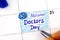 Woman fingers with pen writing reminder National Doctors Day in calendar