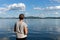 A woman fisherman stands with a fishing rod and catches fish against a blue lake and sky with clouds. Bright shot