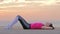 Woman in fitness clothes on the ocean shore doing exercises for the abs