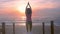 Woman in fitness clothes on ocean shore doing yoga on wooden walkway at sunset
