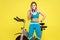 Woman fitness instructor standing near exercise bike and holding megaphone, advertisement gym.