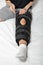 Woman fixing adjustable Velcro orthosis on broken leg sitting in bed. Wearing leg brace after injury. Closeup. Vertical