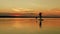 A woman floats on a sappboard in the evening in golden reflections from the sunset on the sky and water