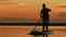 A woman floats on a sappboard in the evening in golden reflections from the sunset on the sky and water