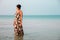 Woman in a floral dress standing in shallow ocean water. Girl in the sea.