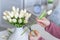 Woman florist cutting stem of tulips flowers with scissors and putting in vase on coffee table. Composing bouque.