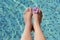 Woman with flower holding feet over water in swimming pool, closeup