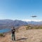 Woman flying drone outdoors with remote control. One person in scenic landscape driving drone filming photographing snowcapped mou