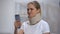 Woman in foam cervical collar reading message on cellphone, feeling pain in neck