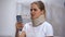 Woman in foam cervical collar reading message on cellphone, feeling pain in neck