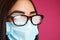 Woman with foggy glasses caused by wearing disposable mask on pink background, closeup. Protective measure during