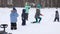 Woman and four children play snowballs during snowfall in winter park