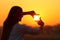 Woman framing sun with fingers at sunset