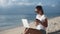 Woman freelancer in sunglasses uses laptop and smartphone for works on beach