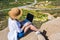 Woman freelancer in tourist clothes and straw hat with a laptop on top of a mountain