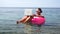 Woman freelancer works on laptop swimming in sea on pink inflatable ring. Happy tourist in sunglasses floating on