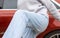 woman in front of lateral door red car in warm pullover blue jeans