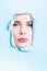 Woman frown face thru blue ripped board