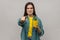 Woman with frowning face holding yellow flower pot with prickly cactus flower and pointing to camera