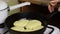 A woman is frying pancakes. Checks the degree of frying using a fork