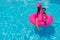 Woman in a fuchsia swimsuit and sunglasses is lounging and sunbathing in a pool with an inflatable flamingo