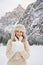 Woman in fur hat holding snow in hands while standing outdoors