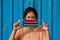 A woman with Gambia flag on hygienic mask in her hand and lifted up the front face on blue background. Tiny Particle or virus