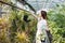 Woman gardener in apron caring potted plant in greenhouse surrounded by plants and pots. Home gardening, love of plants and care.