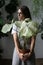 Woman gardener holding flower caladium houseplant with large white leaves in clay pot, looking aside