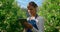 Woman gardener inspecting trees with technological device in big plantation