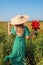 Woman gathered bouquet of poppies flowers walking in summer field. Stylish girl in straw hat admires landscape