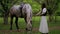 Woman gently petting horse in peaceful woodland setting. Serene moment as woman walks and bonds with horse among trees.