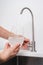 Woman get filtered water from stainless faucet into a glass