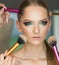 Woman getting powder on skin with brushes, makeup. Hands apply makeup on model face. Woman with young face in beauty