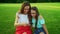 Woman and girl sitting on grass. Mother and daughter looking video on smartphone