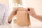 Woman giving paper bag with order to customer in shop, closeup.