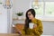 Woman with glasses holding a mug and reading from a notebook on a wooden workbench inside a house.