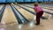 A woman with glasses throws a bowling ball along the track