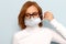 Woman in glasses wearing face medical mask, looking down, isolated on blue background. Flu epidemic, dust allergy