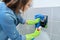 Woman in gloves cleaning and polishing chrome toilet button on tiled wall