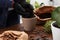 Woman in gloves filling flowerpot with soil at wooden table indoors, closeup. Transplanting houseplants