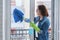 Woman in gloves with microfiber rag sprayed with detergent clean glass window