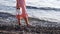 Woman goes barefoot on pebbles in edge of water and holds her white sneakers in hand