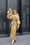 Woman with golden and brown kimono dress and fan in hand before Gucci fashion show, Milan