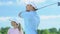 Woman golf beginner player admiring man professionally hitting ball, half-swing