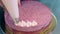 Woman gradually decorates pink biscuit cake top with cream