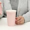 Woman in gray clothes holds a pink ceramic cup, woman sits at a white table, start of the day, morning